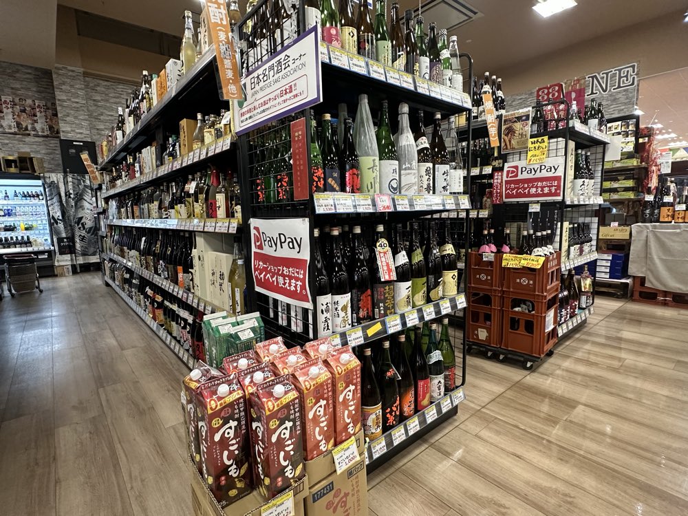 日本名門酒会コーナーなど、日本酒の一升瓶がずらりと並ぶ売り場